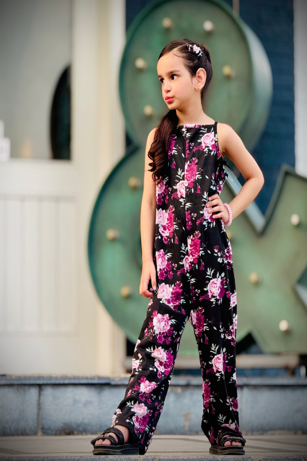 Young girl wearing a floral jumpsuit standing in front of decorative wall.